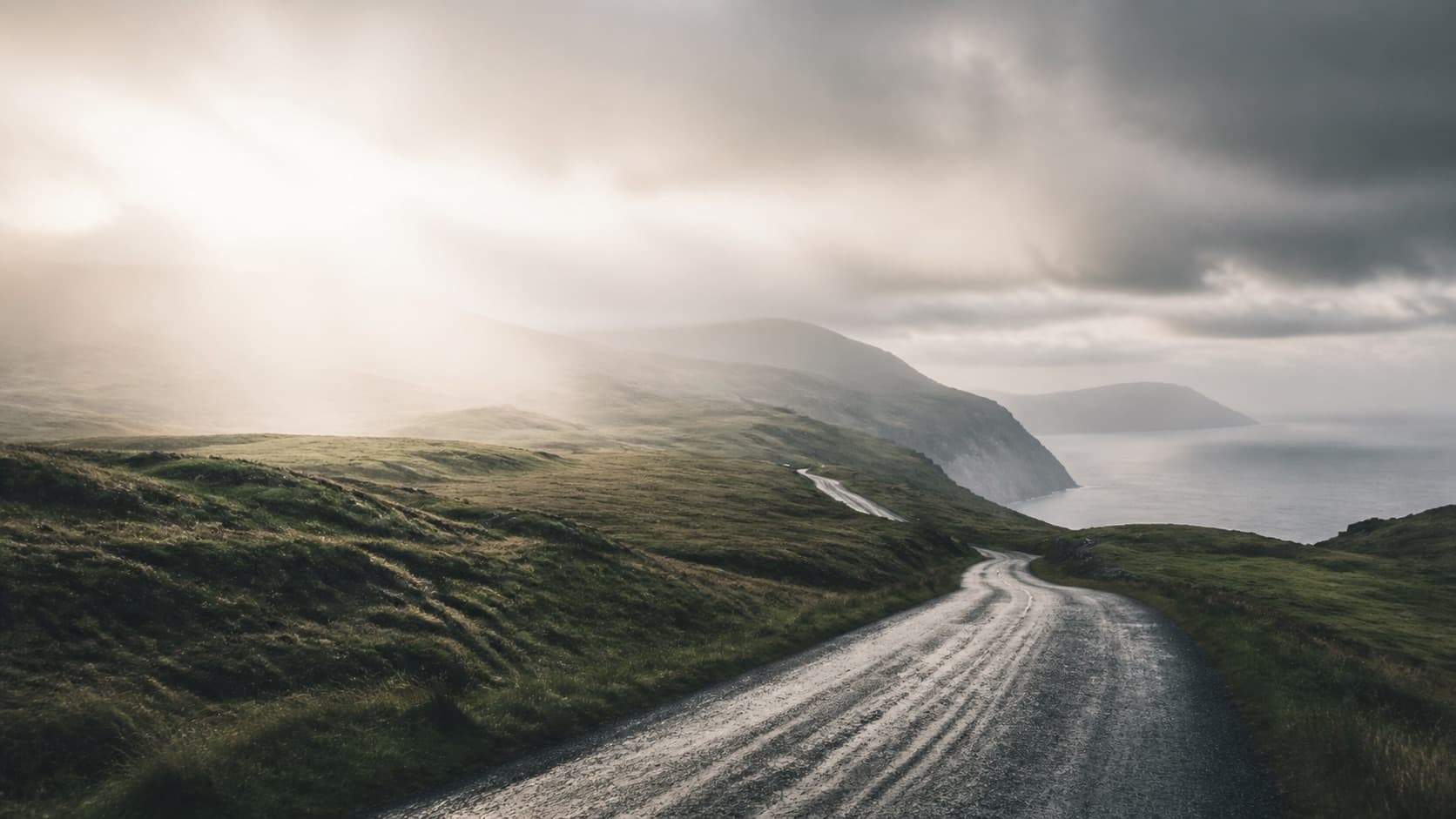 Rainy coastal road through green hills